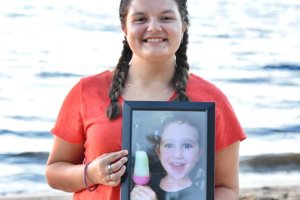 Ansley on the beach holding a framed photo of herself as a child 