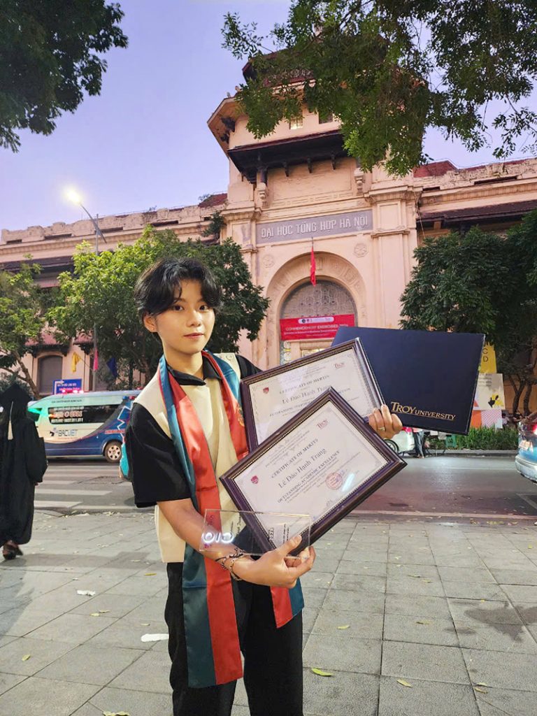 Le Dao Hanh Trang holding her degrees in front of the VNU-UEB campus.
