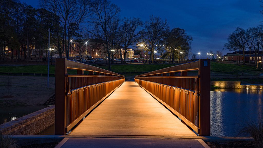 The pedestrian bridge across the Troy University campus lake lighted at dusk.