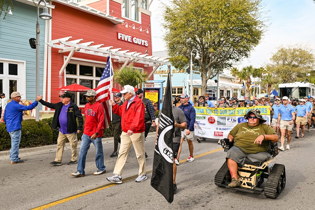 a group of veterans carrying the American flag and the wounded warrior flag lead the walk into Pier Park with the ATO walkers following behind