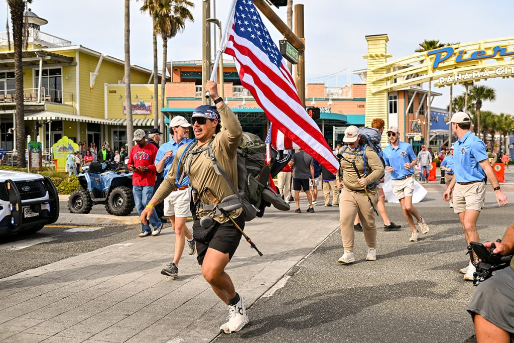 an ATO brother runs with the American flag out of Pier Park towards the beach.