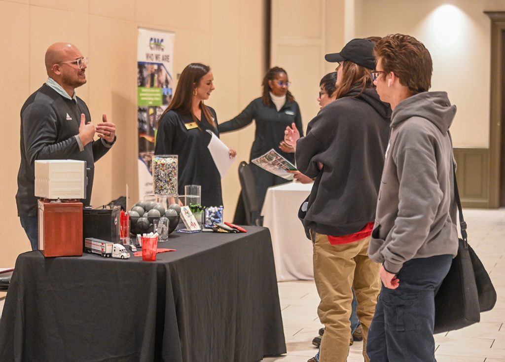 Andrew Womack, far left, speaks with TROY students at the Sanders Lead Company and KW Plastics table.