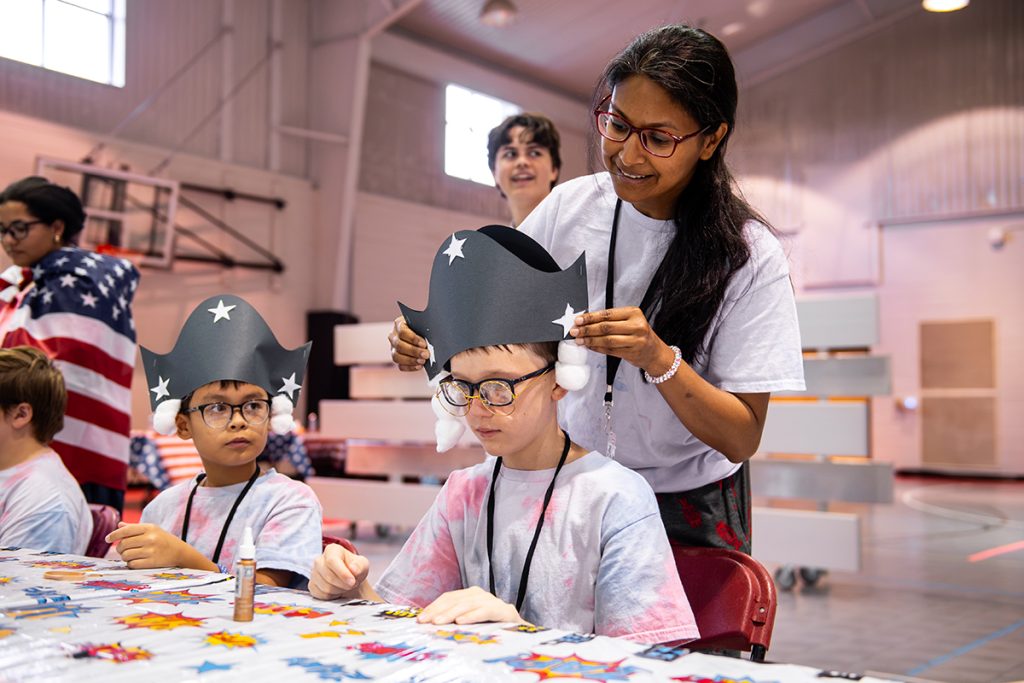 a camp volunteer fixes a black construction paper hat on the head of a civic heroes camp participant.