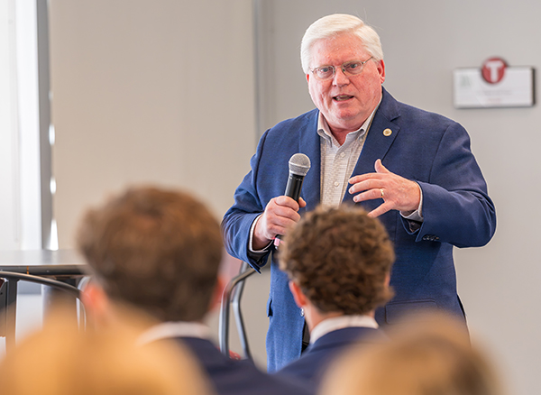 A photo of a man speaking with a microphone